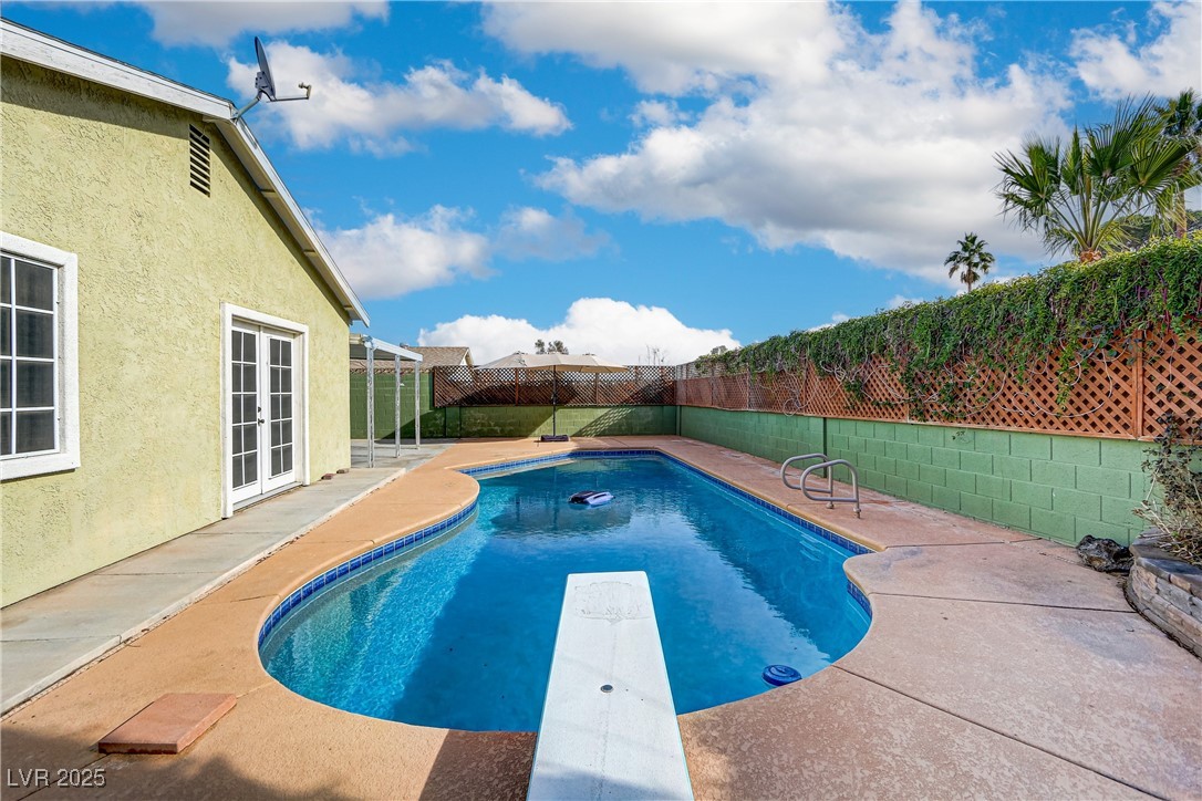 View of swimming pool featuring a fenced backyard, a diving board, a patio, and french doors