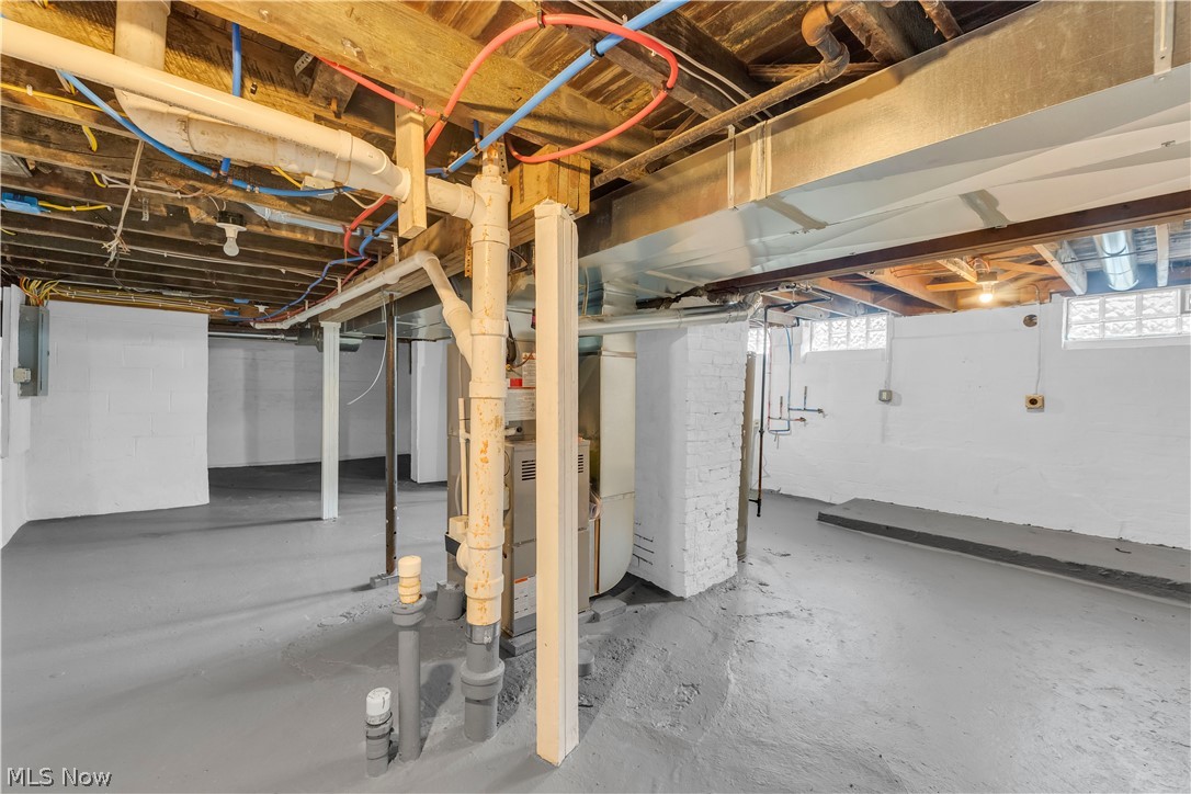 18155 Libby Road Maple Heights, OH 44137 - Photo 27 of 32 Unfinished basement space featuring exposed wood joists, painted concrete flooring, white-painted block walls, and glass block windows