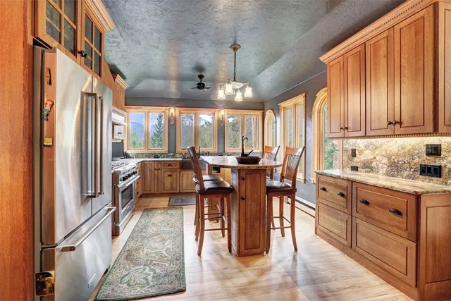 a open kitchen with stainless steel appliances granite countertop a refrigerator a sink dishwasher a dining table and chairs with wooden floor