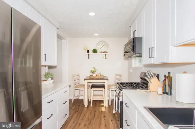 a kitchen with granite countertop a refrigerator a stove a sink dishwasher and white cabinets with wooden floor