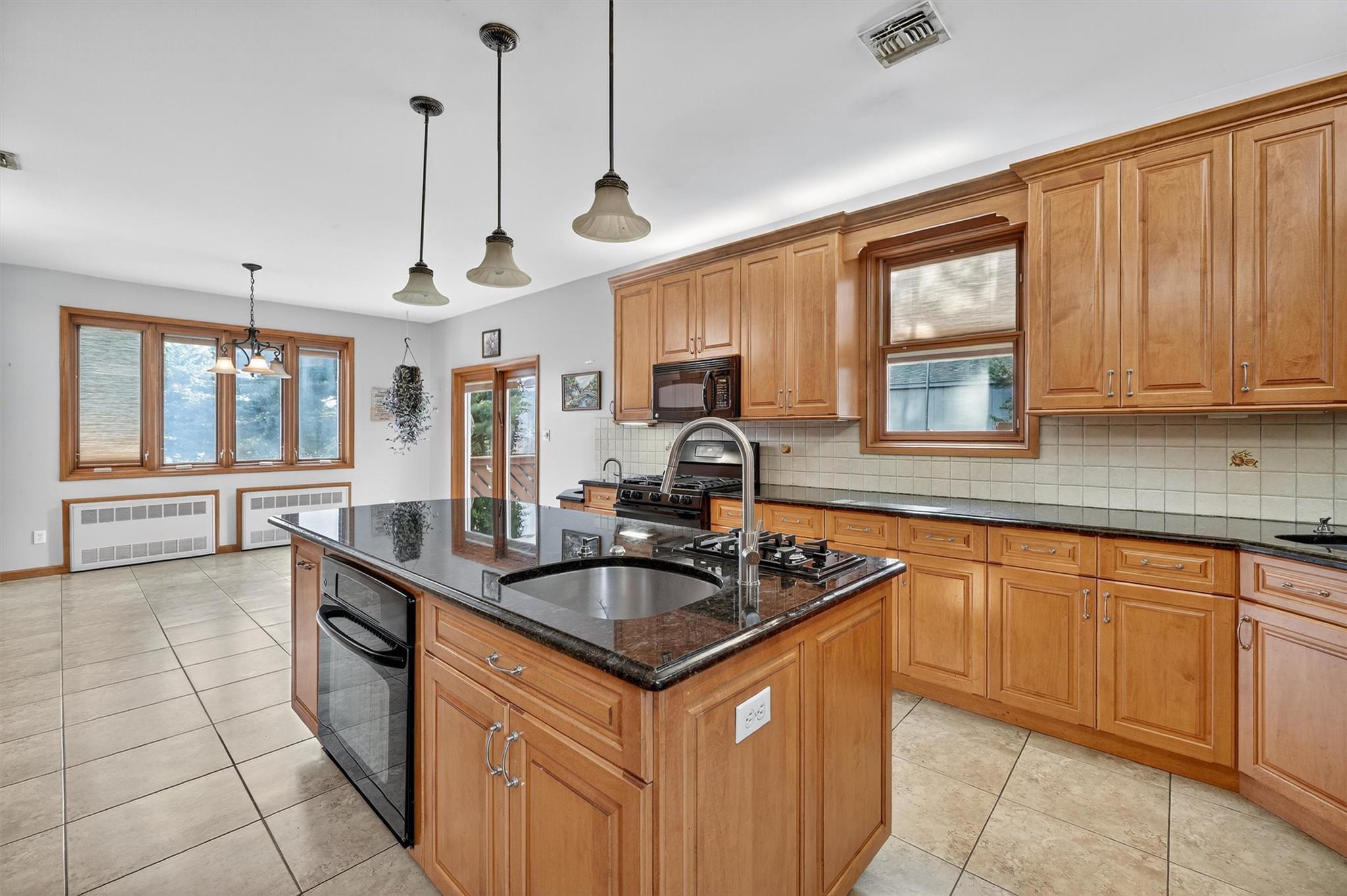 15 Dr Frank Road Spring Valley, NY 10977 - Photo 12 of 50 Kitchen featuring black appliances, radiator, an island with sink, backsplash, and hanging light fixtures