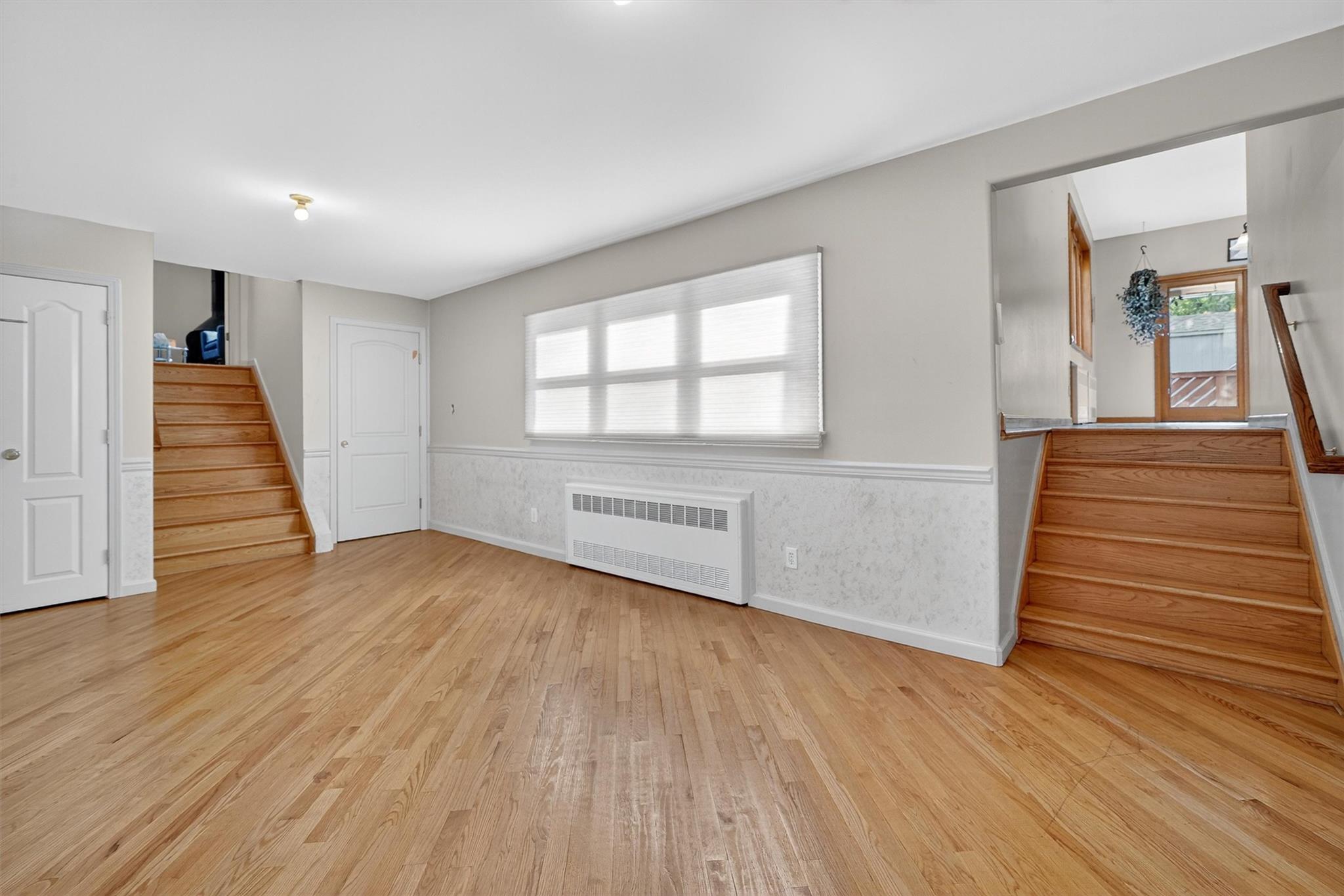 15 Dr Frank Road Spring Valley, NY 10977 - Photo 20 of 50 Unfurnished living room with radiator, stairs, light wood-type flooring, and wainscoting