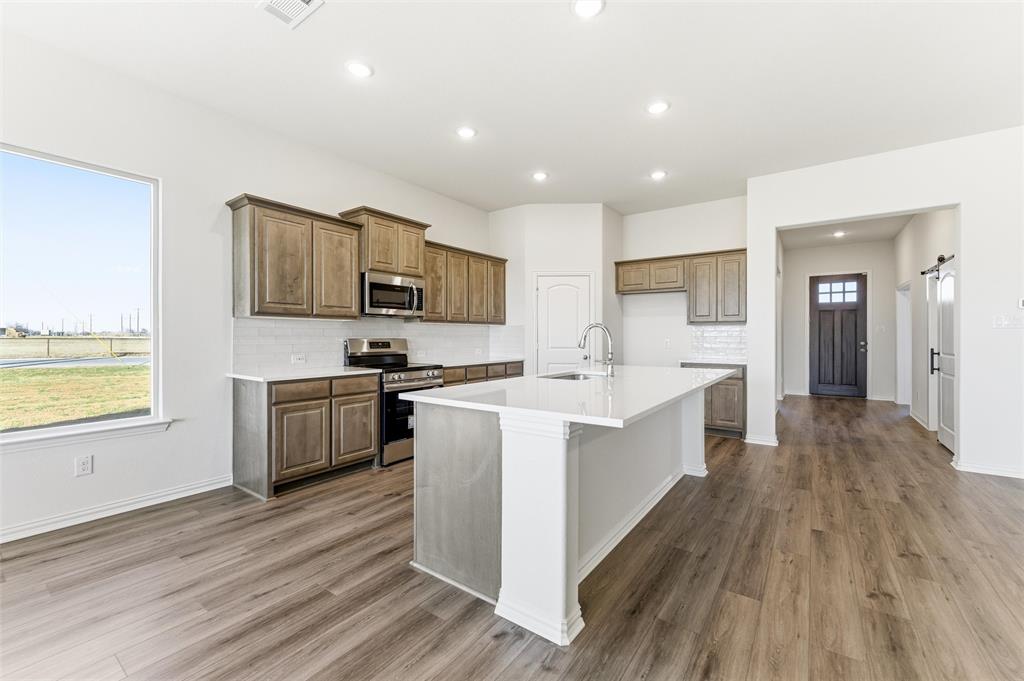 1030 County Road 200 Valley View, TX 76272 - Photo 14 of 27 Kitchen with appliances with stainless steel finishes, an island with sink, brown cabinetry, light wood-style flooring, and recessed lighting