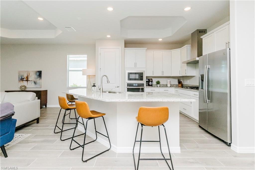 15862 Sugar Hl Drive Babcock Ranch, FL 33982 - Photo 3 of 50 a kitchen with stainless steel appliances kitchen island granite countertop a refrigerator a stove a sink and chairs with wooden floor