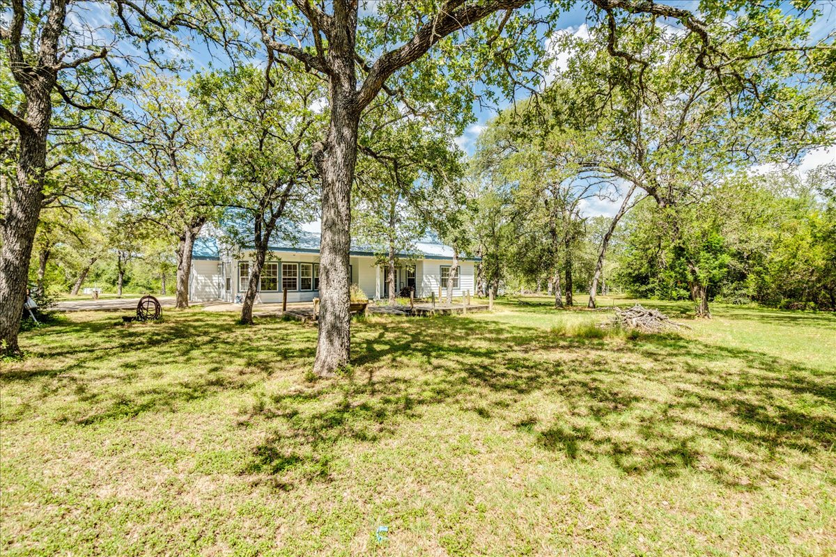 19106 Eyerley Road Manor, TX 78653 - Photo 31 of 40 Mature trees shade a charming white residence nestled amidst a verdant landscape.