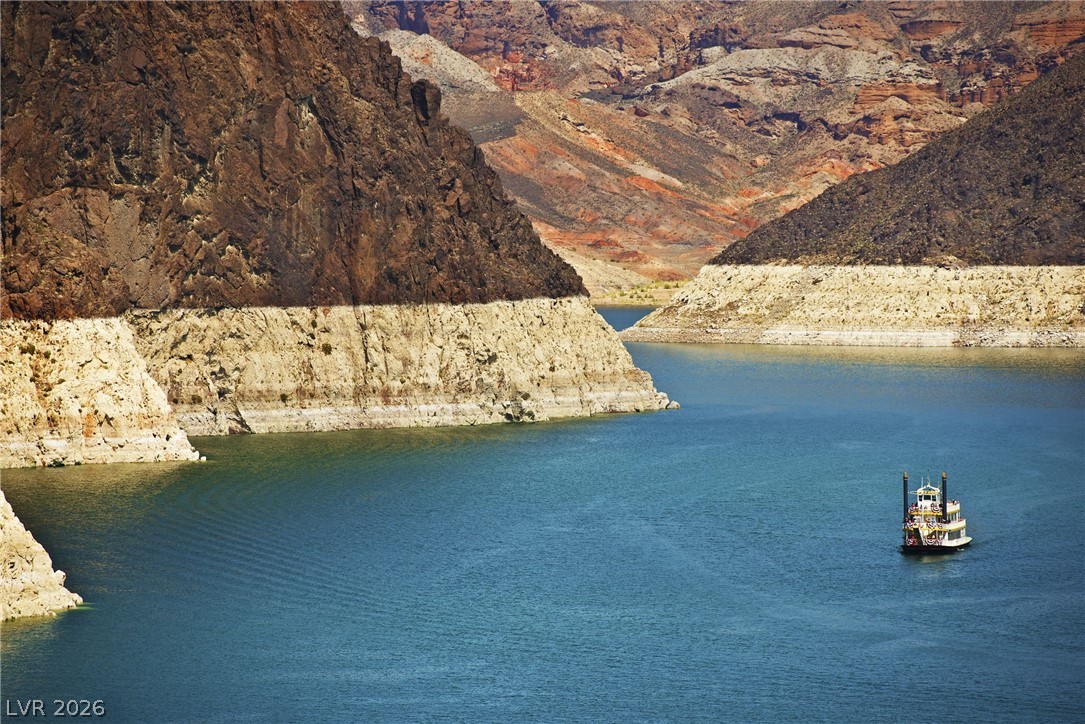 1140 Julie Road Henderson, NV 89002 - Photo 19 of 38 Fifteen minutes to LAKE MEAD! A picturesque boat glides across a tranquil lake, framed by majestic mountains and a vast water view.