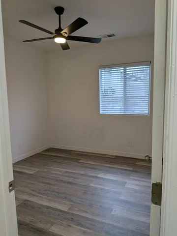 an empty room with wooden floor fan and windows