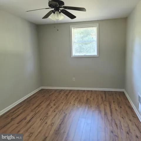an empty room with wooden floor chandelier fan and windows