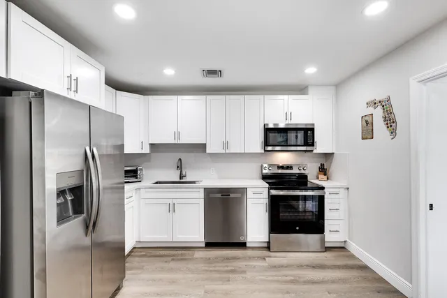 a kitchen with stainless steel appliances granite countertop a refrigerator stove a sink and white cabinets with wooden floor