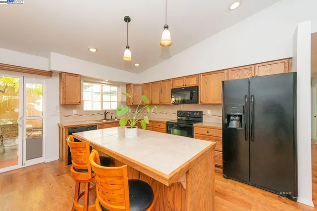 a kitchen with stainless steel appliances granite countertop a refrigerator a stove a sink a dining table and chairs with wooden floor