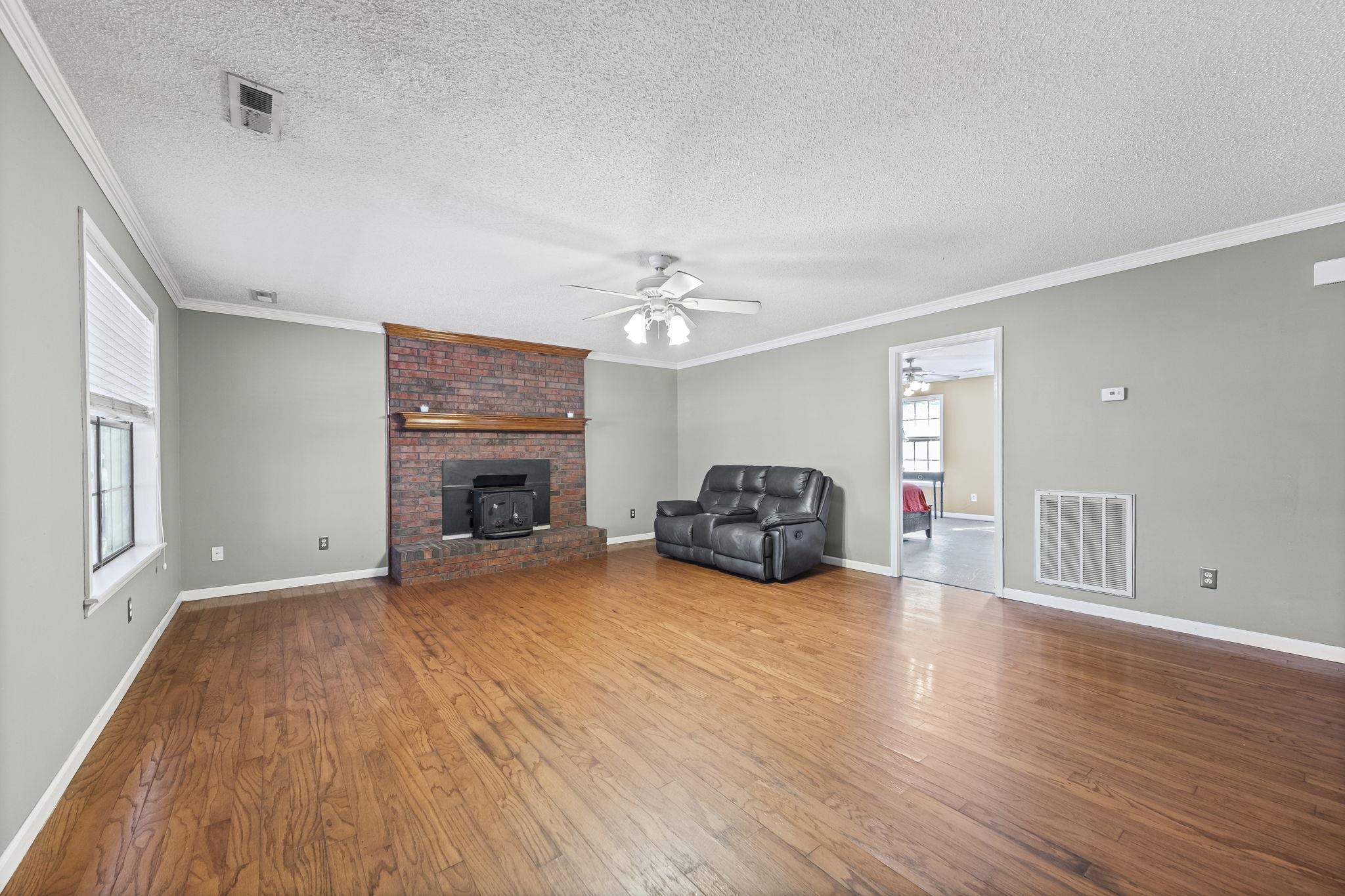 143 Ashley Lane Brighton, TN 38011 - Photo 3 of 37 Unfurnished living room with a textured ceiling, ornamental molding, ceiling fan, dark wood-style flooring, and a wood stove