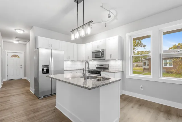 a kitchen with stainless steel appliances granite countertop a refrigerator a sink dishwasher a stove and white countertops with wooden floor