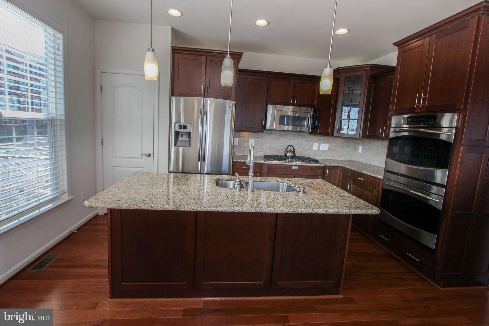 22629 Hawkbill Square Ashburn, VA 20148 - Photo 17 of 30 a kitchen with kitchen island granite countertop a sink and a stove top oven with wooden floor