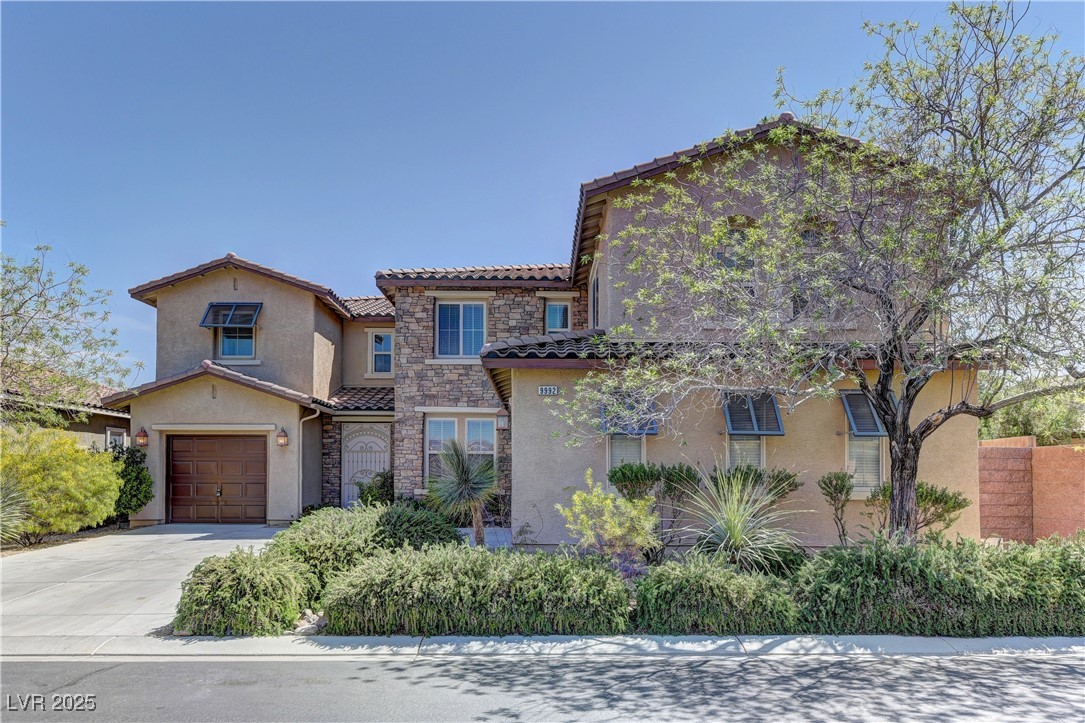 Mediterranean / spanish-style house with a tiled roof, stucco siding, stone siding, an attached garage, and concrete driveway