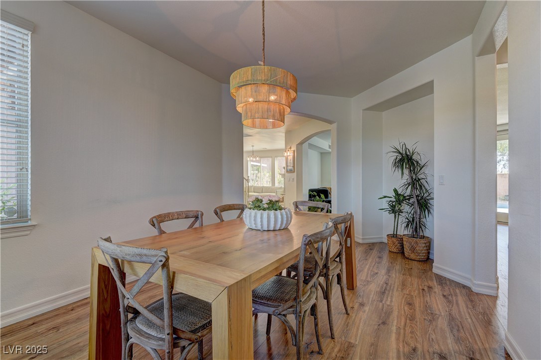 9992 South Sky Parlor Road Las Vegas, NV 89178 - Photo 6 of 42 Dining area featuring light wood finished floors, arched walkways, a healthy amount of sunlight, and an inviting chandelier