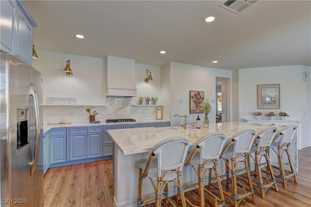 9992 South Sky Parlor Road Las Vegas, NV 89178 - Photo 9 of 42 Kitchen featuring light wood-type flooring, blue cabinetry, a breakfast bar, stainless steel appliances, and premium range hood