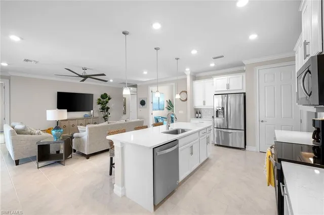a large kitchen with stainless steel appliances lots of white furniture a sink and a refrigerator