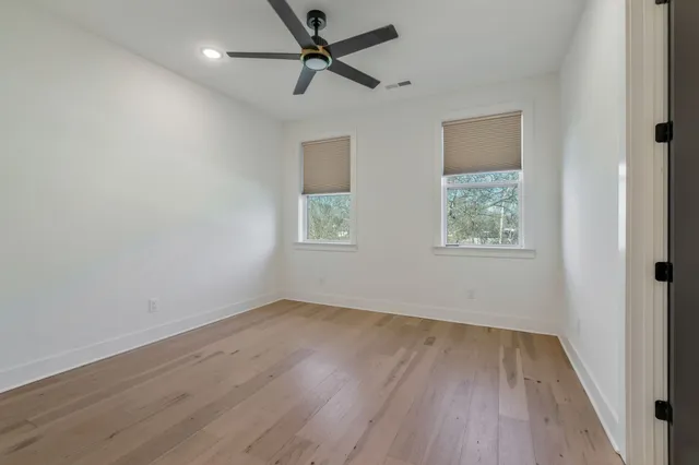an empty room with wooden floor ceiling fan and windows