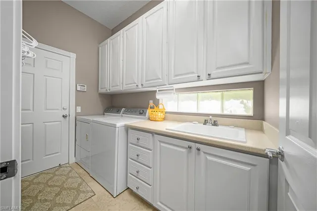 a utility room with stainless steel appliances granite countertop a sink and dishwasher with white cabinets