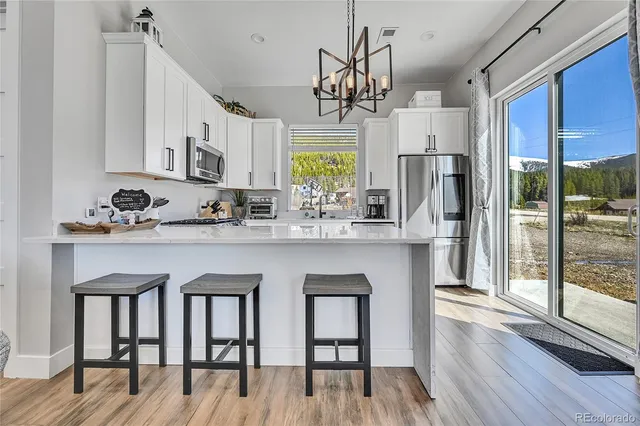 a kitchen with stainless steel appliances granite countertop a refrigerator a sink dishwasher a stove and white cabinets with wooden floor