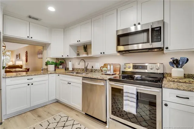 a kitchen with stainless steel appliances granite countertop white cabinets a sink and dishwasher a stove top oven with wooden floor