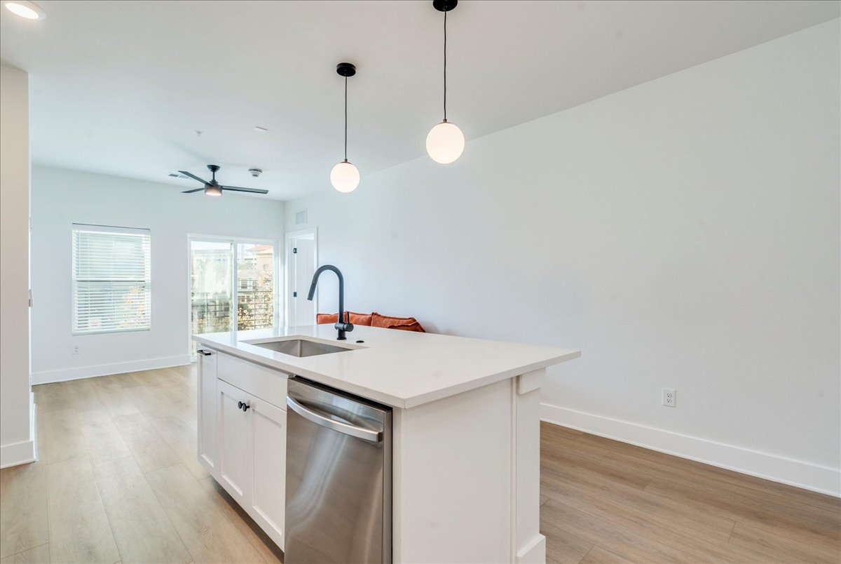 3000 Duval Street, Unit 102 Austin, TX 78705 - Photo 2 of 40 Kitchen featuring white cabinetry, dishwasher, pendant lighting, light wood finished floors, and a kitchen island with sink