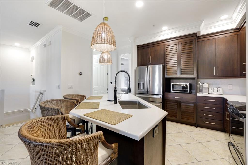 9072 Rialto Street, Unit 6302 Naples, FL 34113 - Photo 4 of 17 Kitchen featuring dark wood finish cabinets, stainless steel appliances, crown molding, light tile patterned floors, and an island with sink