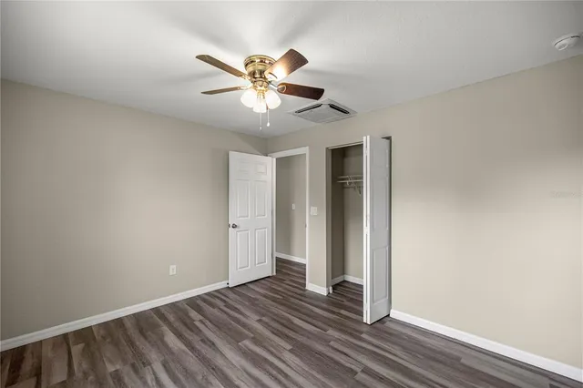 an empty room with wooden floor fan and windows