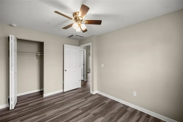 an empty room with wooden floor fan and windows
