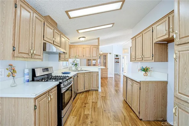 a kitchen with stainless steel appliances granite countertop a stove top oven a refrigerator a sink dishwasher and white cabinets with wooden floor