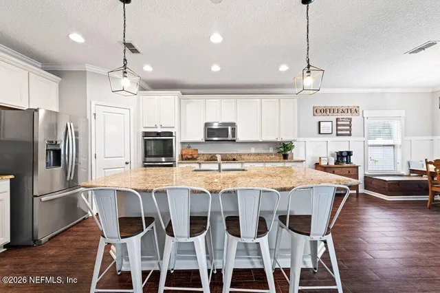 a kitchen with stainless steel appliances granite countertop a dining table chairs refrigerator and microwave