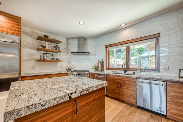 a view of a kitchen with granite countertop center island a wooden floor stainless steel appliances and windows