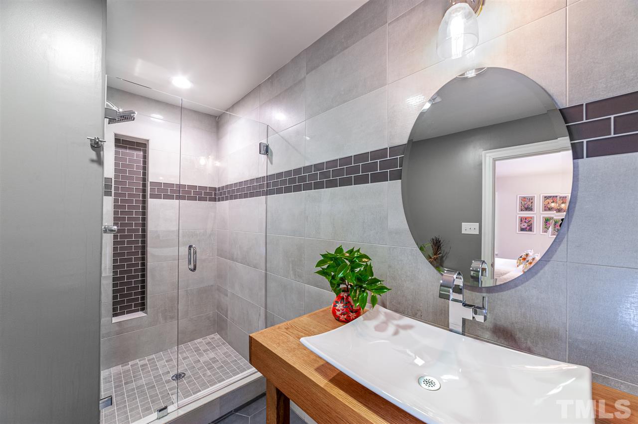 2251 Cranford Road Durham, NC 27705 - Photo 23 of 30 The sleek Second Bedroom Ensuite modern bathroom has floor to ceiling marble with accent tile, hinged frameless shower door, rain shower head, vessel sink and tile flooring.