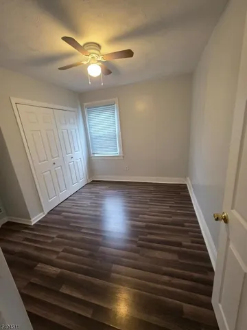a view of an empty room with wooden floor and a ceiling fan