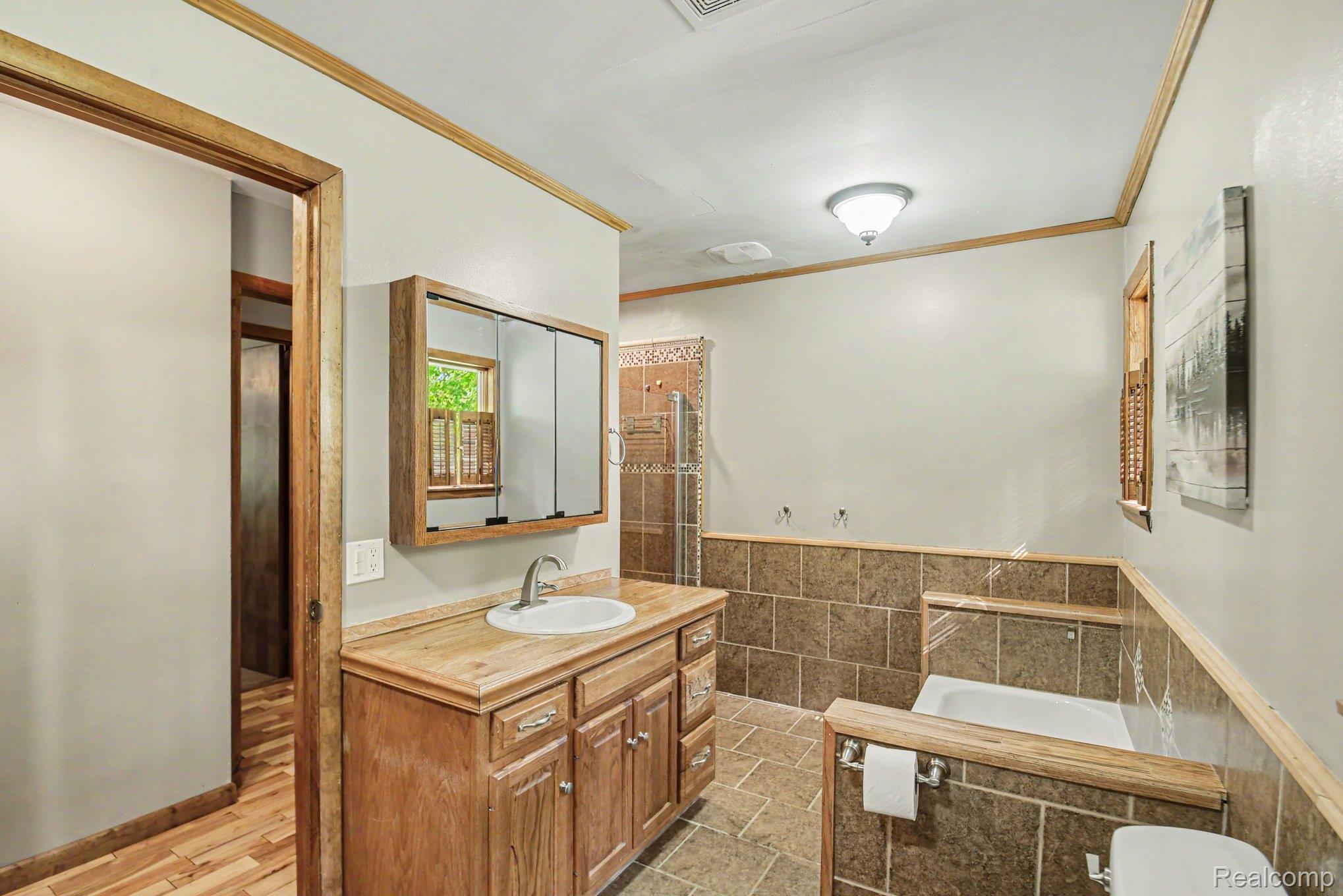1646 Boy Scout Road Caro, MI 48723 - Photo 14 of 28 Bathroom featuring a wood-finish vanity with an integrated sink and chrome faucet, tile wainscoting, and a built-in tub with tile surround