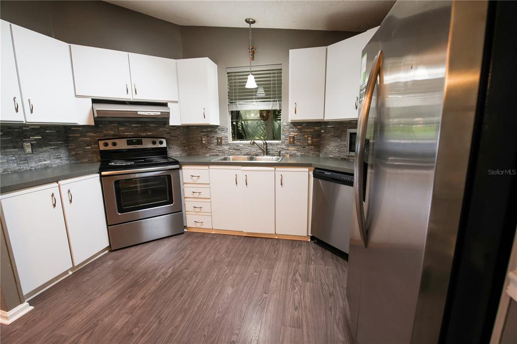 912 Orchid Street The Villages, FL 32159 - Photo 4 of 20 a kitchen with stainless steel appliances kitchen island granite countertop a stove a refrigerator and a wooden floor