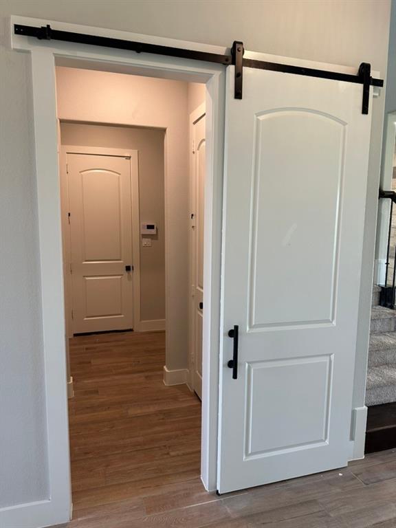 390 Cobb Road Leonard, TX 75452 - Photo 9 of 26 White paneled barn door with black hardware, opening to a hallway featuring wood-finish flooring and white interior doors with black handles