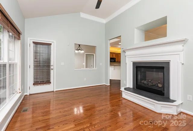 a view of an empty room with wooden floor fireplace and a window