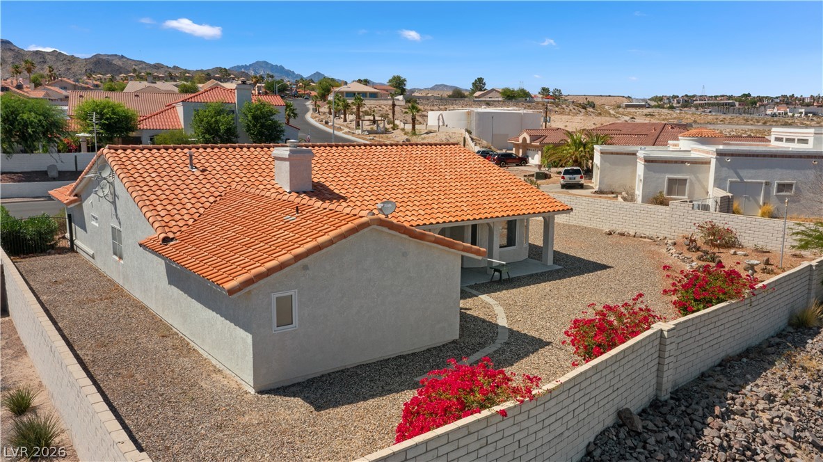 2055 Cholla Way Laughlin, NV 89029 - Photo 78 of 87 Red-tiled roofing crowns this stucco residence, nestled amidst a landscape of low-maintenance gravel and vibrant red flora.