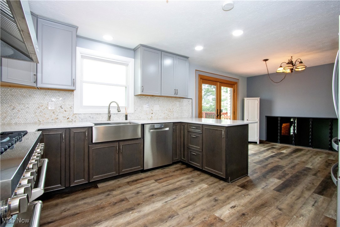 Kitchen featuring a peninsula, appliances with stainless steel finishes, wall chimney exhaust hood, backsplash, and dark wood-style floors