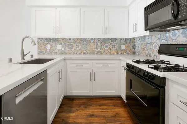 a view of a kitchen with stainless steel appliances a kitchen island wooden floors and a chandelier