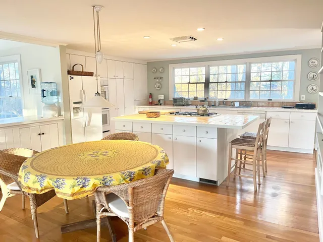 a dining hall with stainless steel appliances kitchen island granite countertop a dining table chairs and a refrigerator