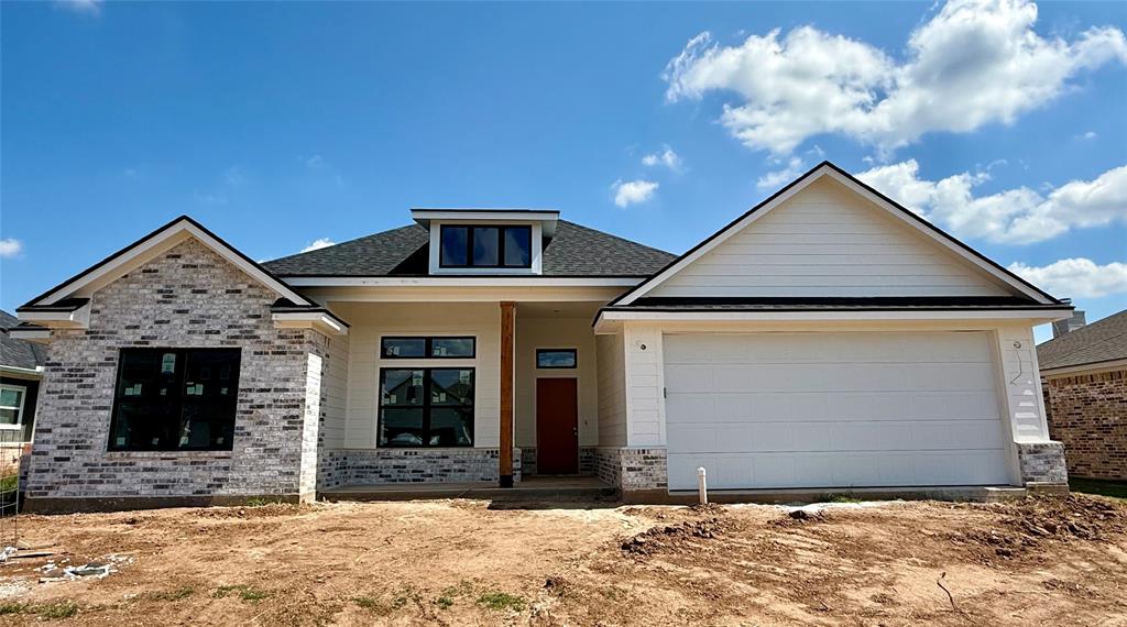 View of front of house with covered porch, brick siding, roof with shingles, and a garage
