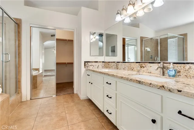 a bathroom with a granite countertop double vanity sink a mirror and a shower
