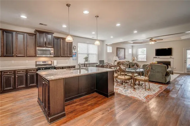 a kitchen with stainless steel appliances granite countertop a stove top oven a sink dishwasher a dining table and chairs with wooden floor