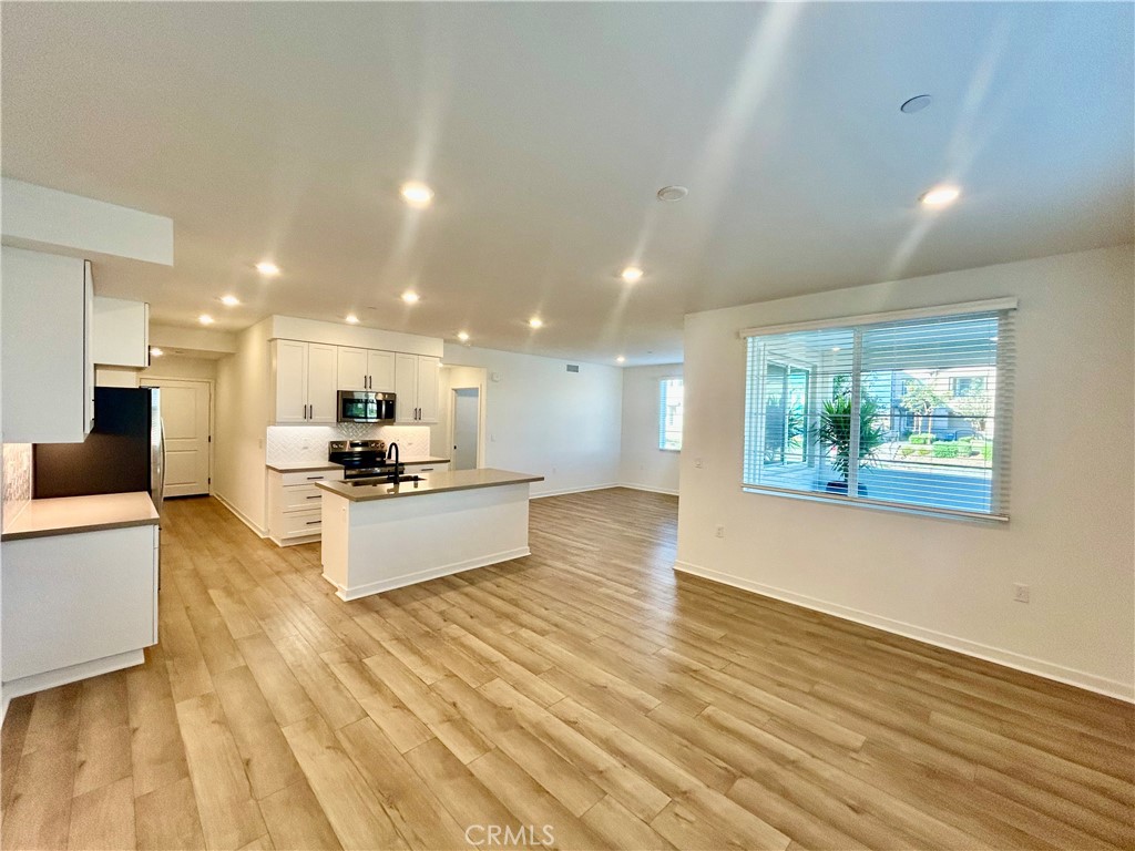 6114 Valentina Way, Unit 101 Eastvale, CA 92880 - Photo 19 of 23 a large living room with stainless steel appliances kitchen view and wooden floor