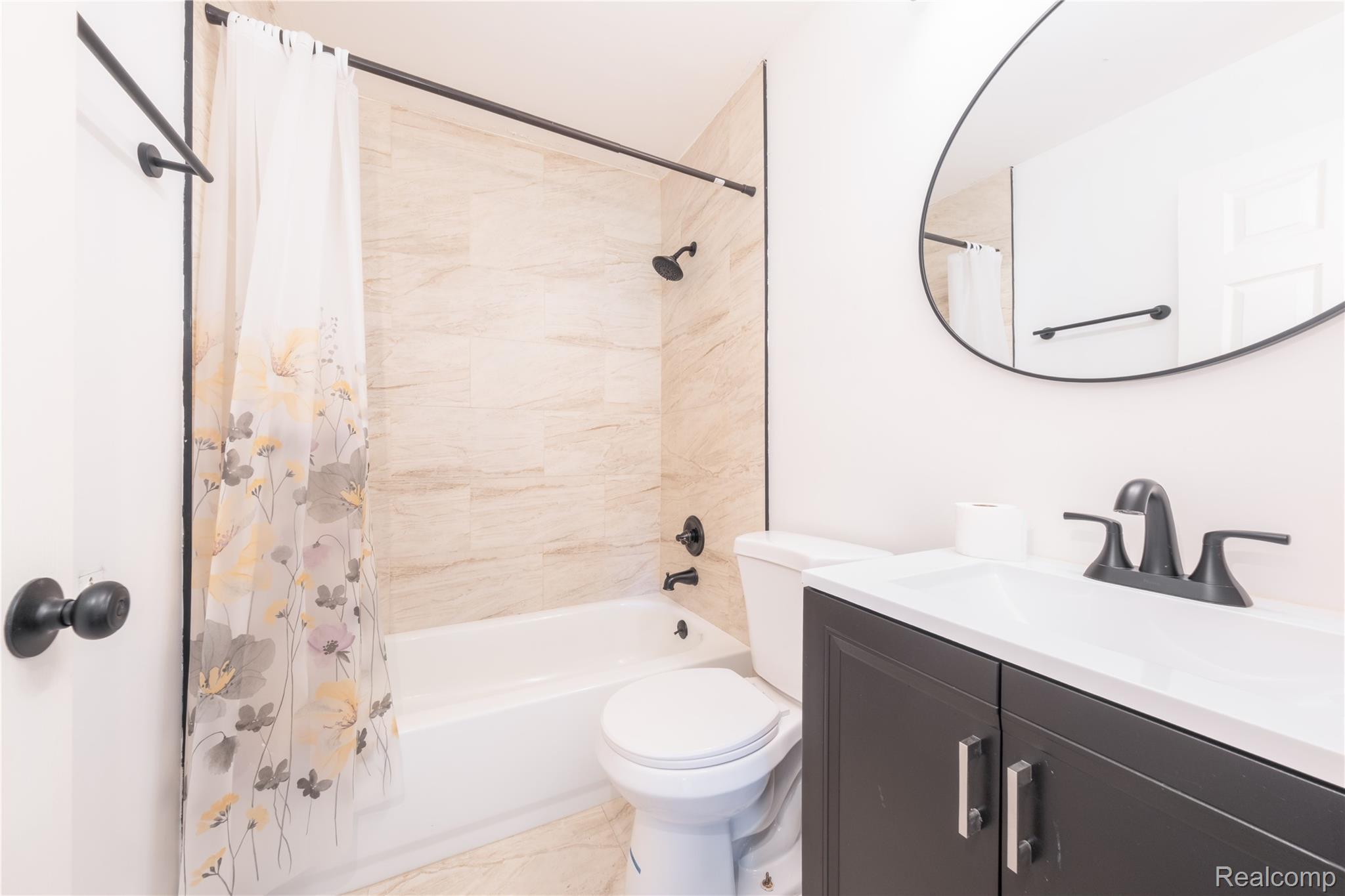 3065 South Commerce Road, Unit 9 Walled Lake, MI 48390 - Photo 12 of 15 Bathroom featuring a white bathtub, tiled shower surround, dark vanity with white countertop, and a contemporary oval mirror