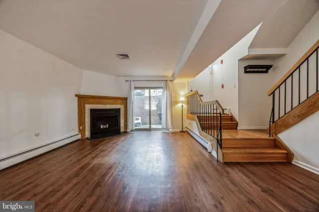 a view of an empty room with wooden floor a fireplace and a window