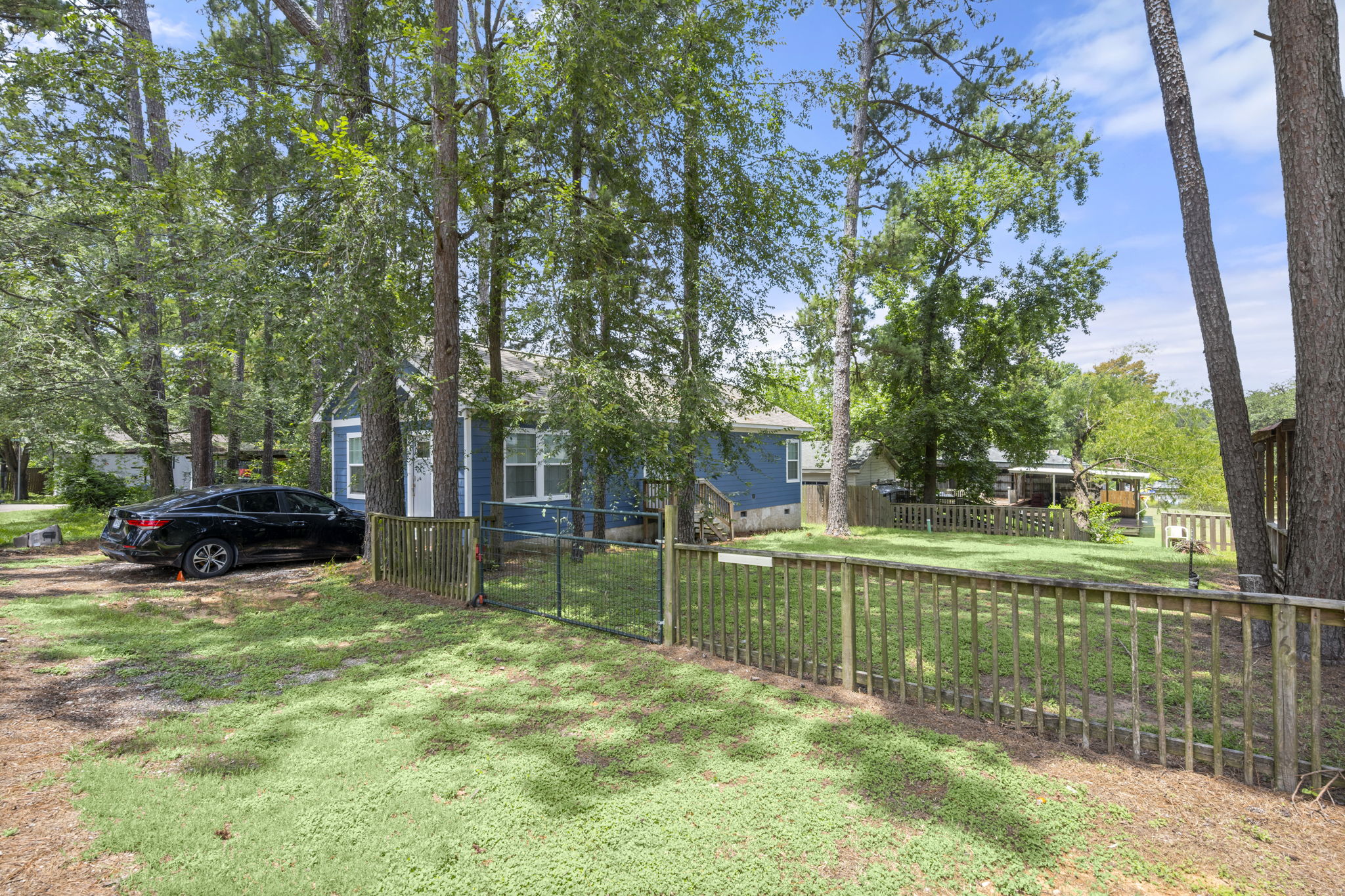 9649 Warm Spring Willis, TX 77318 - Photo 7 of 30 A quaint blue dwelling nestles among mature trees, featuring a fenced yard for privacy.