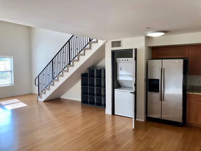 a view of a livingroom with wooden floor staircase and kitchen space a refrigerator